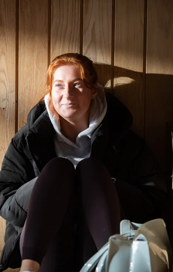 Student sitting in sunlight on wooden steps at Glasgow Kelvin College Springburn campus, wearing casual clothes and smiling softly Student sitting in sunlight on wooden steps at Glasgow Kelvin College Springburn campus, wearing casual clothes and smiling softly
